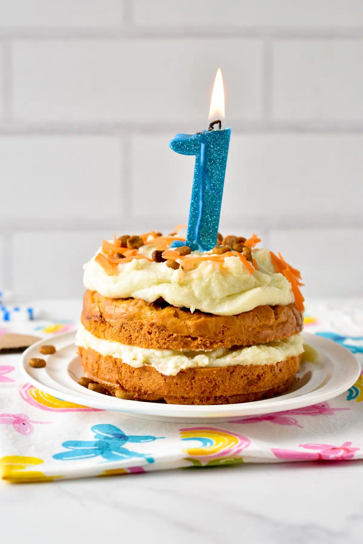 A 2-layer small-serve Dog Cake Recipe frosted with mashed potato frosting and topped with grated carrots, dog treats, and a one year old blue candle.