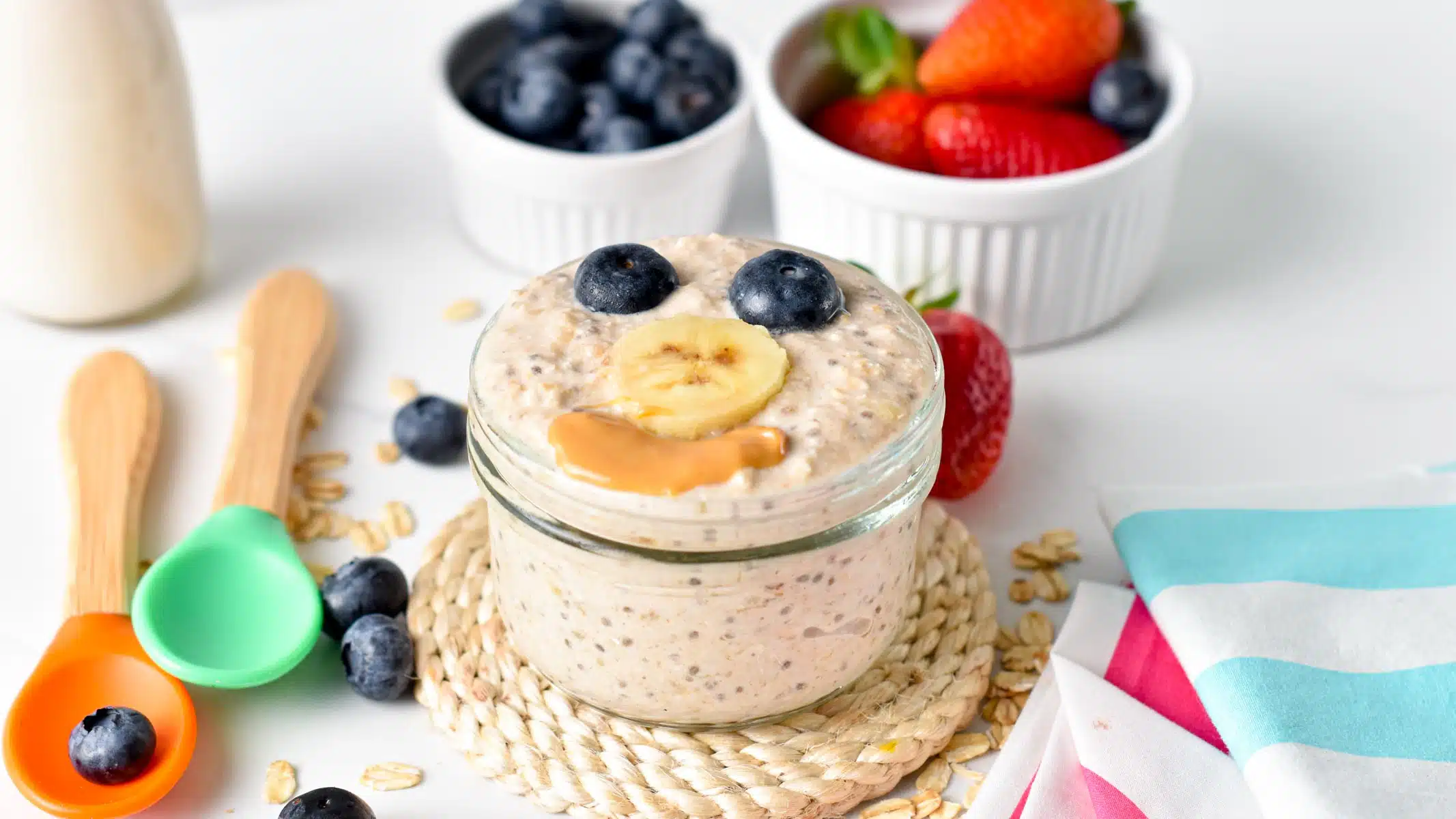 a glass jar filled with Overnight Oat for Baby topped with banana blueberries and peanut butter