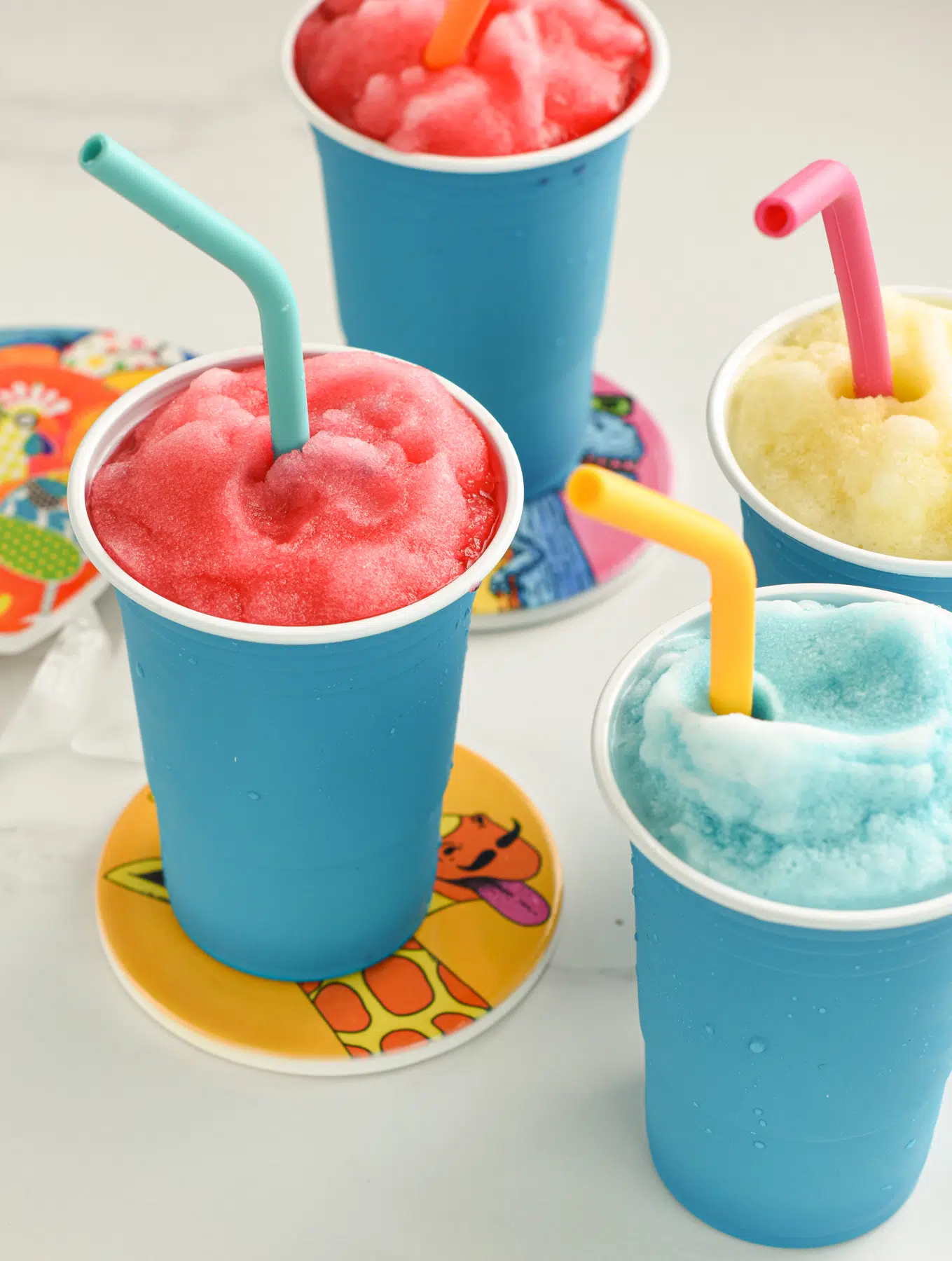 Four Slushies in tall blue cups with color silicone straws.